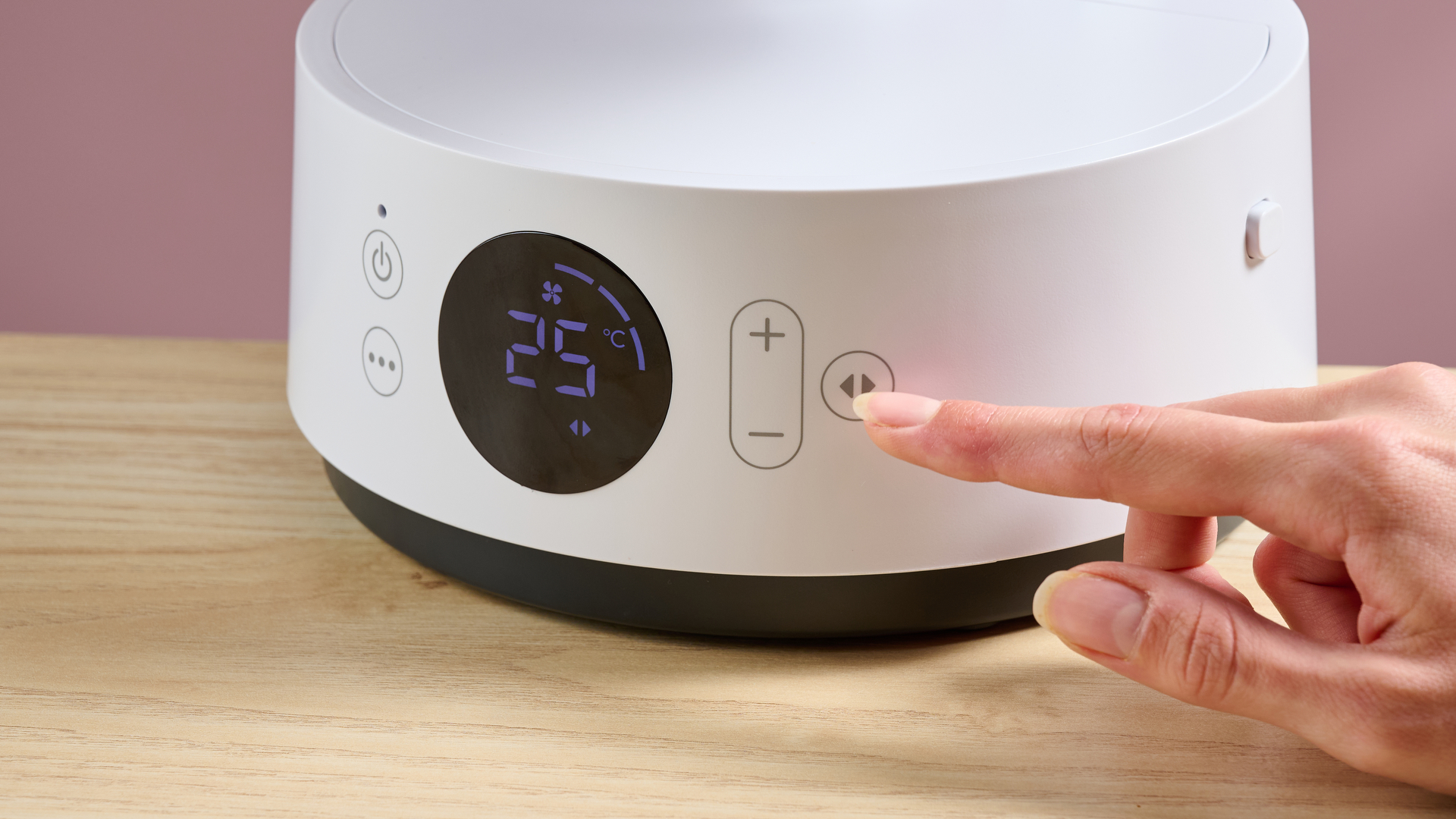 A woman is pressing the button to get the fan to oscillate.